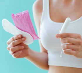 Close-up of young woman with a menstrual compress and a tampon on blue background.